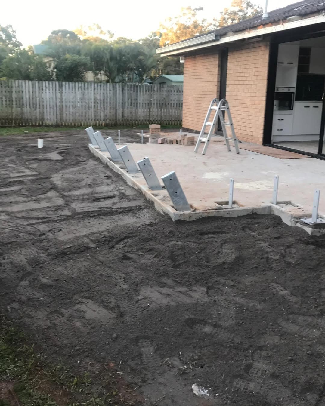 Concrete slab and angled post brackets prepared beside the existing brick home