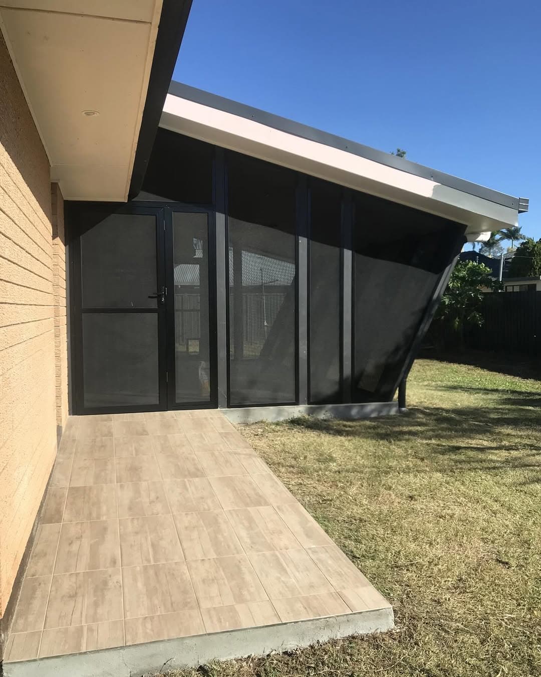Finished garden enclosure with angled posts, a dark screen door and tiled entrance beside the brick home