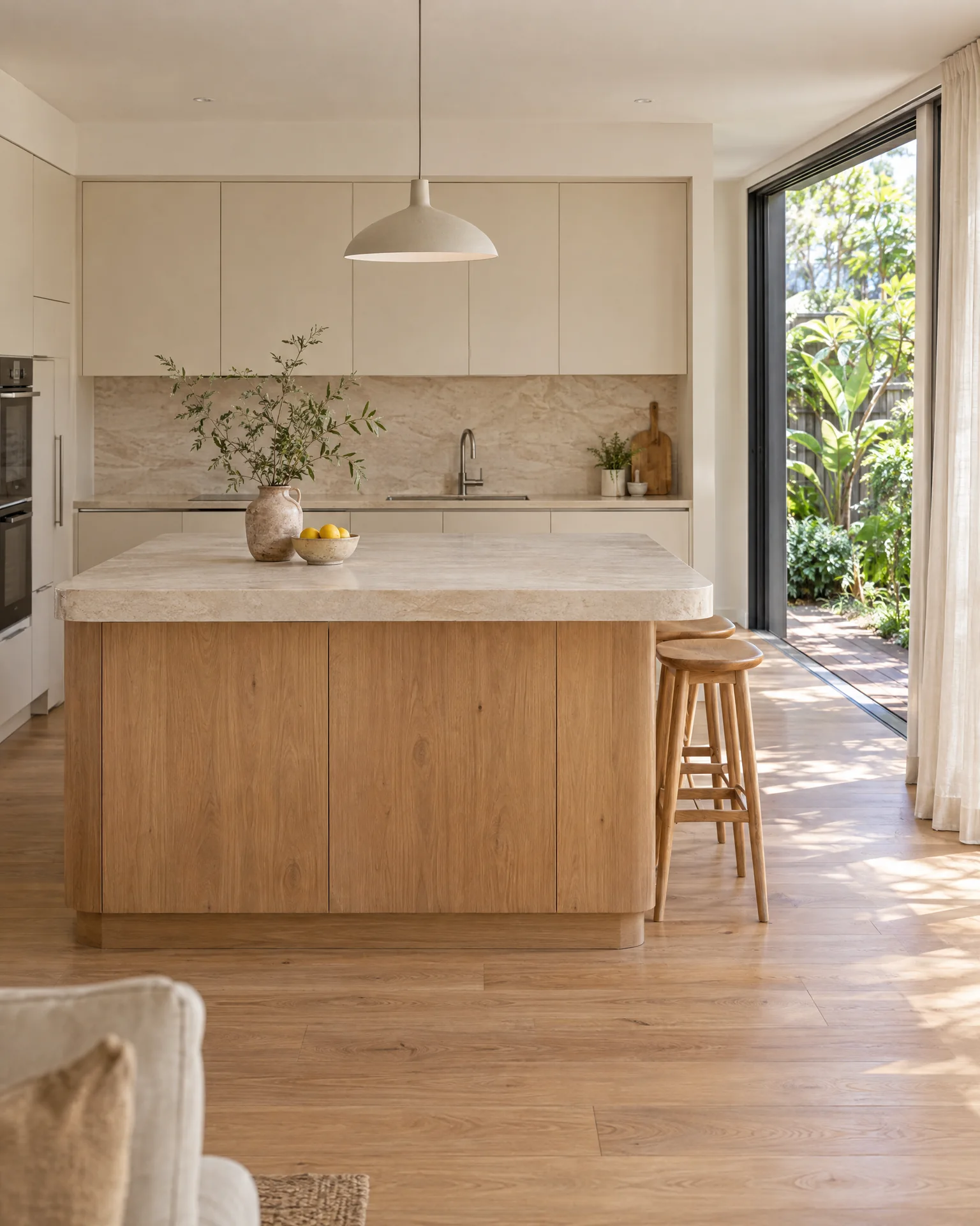 A warm oak kitchen with a pale stone island opening onto a leafy garden